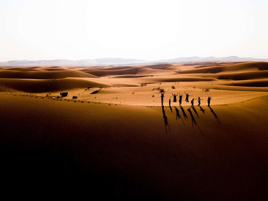 Aerial view of a group jumping in the Iranian desert at sunset with dramatic shadows and sand dunes.